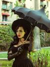 Micheline Pitt stands in a garden holding a black umbrella while modeling the Southern Gothic bustier top in black.