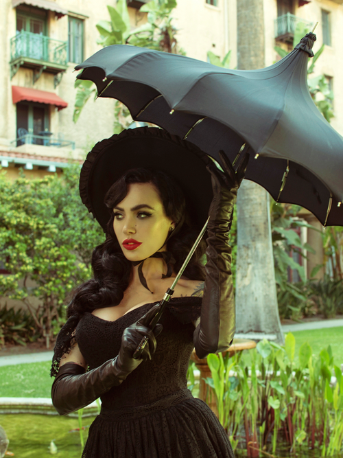 Micheline Pitt stands in a garden holding a black umbrella while modeling the Southern Gothic bustier top in black.