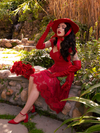 Micheline Pitt pushing the brim of her hat up while modeling a red low-cut top and crimson red gothic skirt.