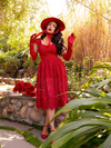 Micheline Pitt standing in her garden while wearing the Southern Gothic Skirt in Crimson with matching top, hat and shoes. All gothic style clothing items from La Femme en Noir.