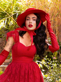 Micheline Pitt staring at the camera while wearing a crimson red bustier top paired with elbow length vinyl gloves and matching hat.