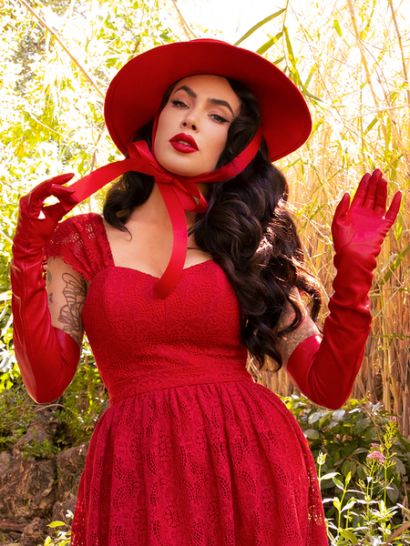 Micheline Pitt tugging on the tie on her crimson red hat to complement her Southern Gothic Bustier Top in Crimson. 