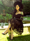 Micheline Pitt sitting in a lush and quaint garden area wearing the Southern Gothic Skirt in Black while sitting on a stone bench.