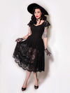 Micheline Pitt standing with her hand on her skirt modeling the Southern Gothic skirt in black petite by La Femme En Noir.