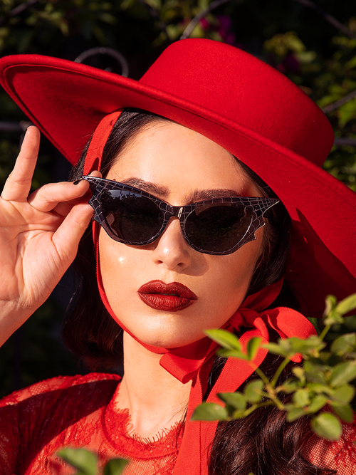 Model Ashley wearing an all red goth style outfit with stunning accent Vamp Batwing Sunglasses in Smoke Spider Web to pull the entire look together.