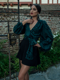 Aliza wearing the Georgette Wrap Blouse in Serpentine Print by Natalie Hall while hanging onto a rod iron vintage gate.