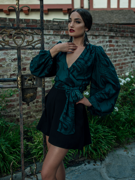 Aliza wearing the Georgette Wrap Blouse in Serpentine Print by Natalie Hall while hanging onto a rod iron vintage gate.