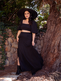 Ashley standing while modeling the Thistle Two Piece Set in Black Chiffon she's paired with a black sunhat - all items from goth glamour brand La Femme en Noir.