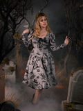 Tip-toeing through a cemetery, Linda models the Sleepy Hollow Gothic Tales Toile Swing Dress in Grey from gothic glamour clothing company La Femme en Noir.