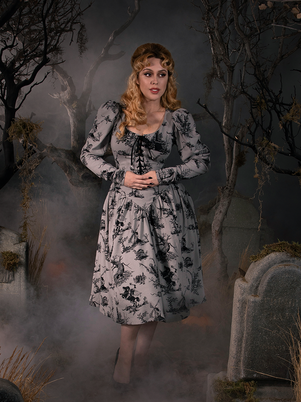 Linda standing with her hands clasped in front of her wearing a grey goth style dress from La Femme en Noir.