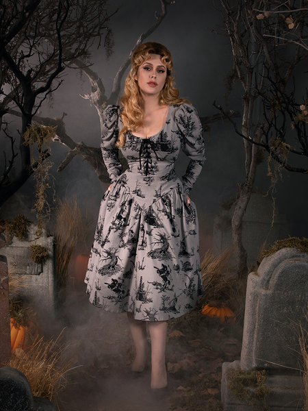 With her hands behind her back, Linda shows off the Sleepy Hollow Gothic Tales Toile Swing Dress in Grey from goth style clothing company La Femme en Noir.