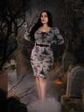 Rachel Sedory with her hands on her waist poses in the Sleepy Hollow Gothic Tales Toile Wiggle Dress in Grey. 