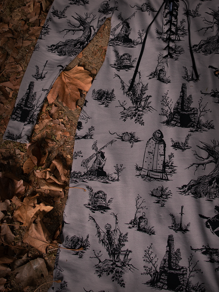 Close up of the Sleepy Hollow Gothic Tales Toile Wiggle Dress in Grey laying flat on a bed of leaves.