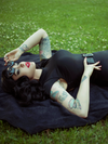 Laying down on the grass on top of a black towel, Micheline Pitt models the Glamour Ghoul Swimsuit.