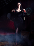 Heather Clark wearing the Vampira® Show Gown in a smoky room with a red velvet couch.