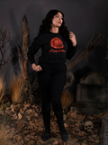Full length shot of Micheline Pitt wearing an all black outfit including the all new Sleepy Hollow™ Van Garrett Wax Seal Cropped Sweatshirt.