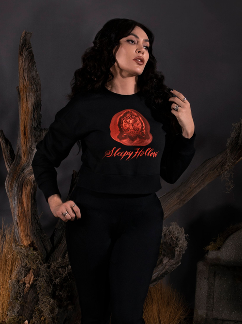 Micheline Pitt standing in front of a dead tree next to a tombstone, wears the Sleepy Hollow™ Van Garrett Wax Seal Cropped Sweatshirt from gothic glamour brand La Femme en Noir.