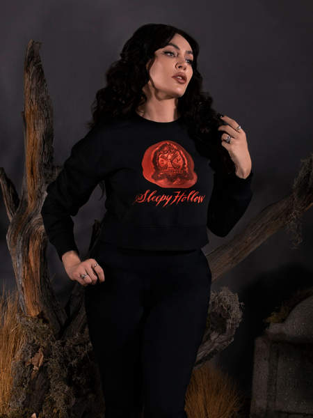 Micheline Pitt standing in front of a dead tree next to a tombstone, wears the Sleepy Hollow™ Van Garrett Wax Seal Cropped Sweatshirt from gothic glamour brand La Femme en Noir.
