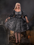 Looking off camera while standing in a cemetery, Micheline models the gothic Sleepy Hollow™ Lady Van Tassel Guipire Lace Dress by La Femme En Noir.