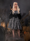Looking into the distance, Micheline models the Sleepy Hollow™ Lady Van Tassel Guipire Lace Dress with elbow length black gloves.