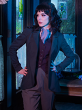 Stephanie places her hands on her hips while wearing Tim Burton's CORPSE BRIDE™ Victor Peplum Blazer in Spruce Green in a dimly lit old Victorian home.