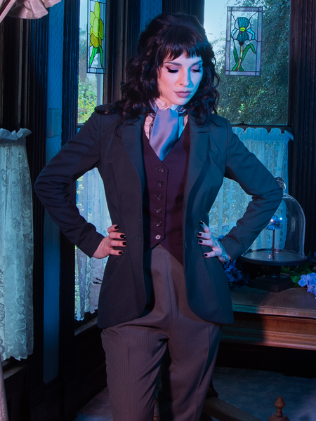 Stephanie looks down at the floor while posing in Tim Burton's CORPSE BRIDE™ Victor Peplum Blazer in Spruce Green from gothic retro clothing company La Femme en Noir.