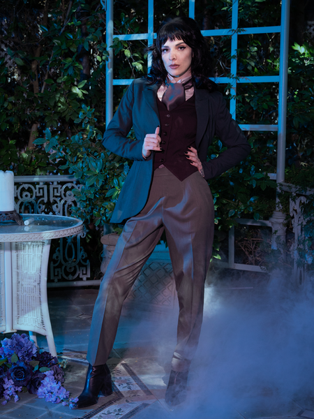 Stephanie stands in a smoky garden setting looking like she stepped right out of a Victorian painting while wearing an olive green jacket and the Tim Burton's CORPSE BRIDE™ Victor Pinstripe Pant in Dusty Olive.