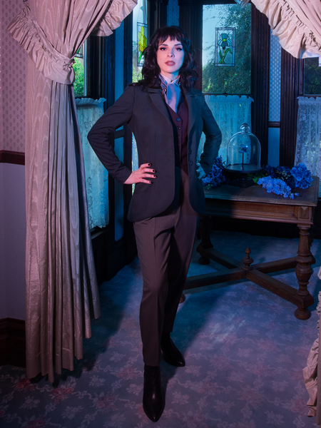 Stephanie standing in an entryway of a old Victorian home as she models the an old, Victorian outfit highlighted by the Tim Burton's CORPSE BRIDE™ Victor Pinstripe Pant in Dusty Olive.