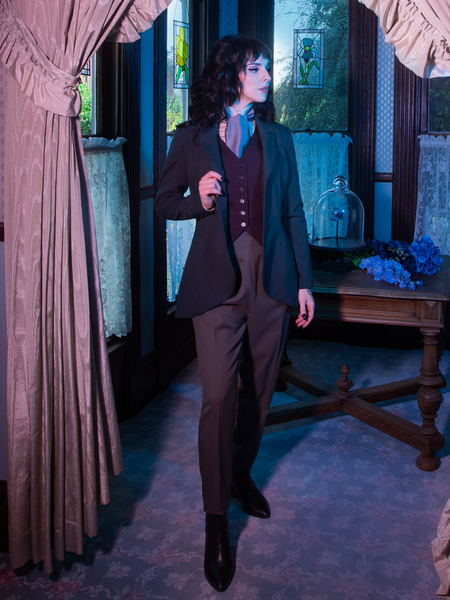 A profile shot of Stephanie standing in front of the foyer of an old Victorian house while wearing an old, Victorian outfit including the Tim Burton's CORPSE BRIDE™ Victor Pinstripe Pant in Dusty Olive from retro goth clothing company La Femme en Noir.