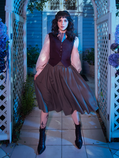 Stephanie standing under an outdoor archway wearing the Tim Burton's CORPSE BRIDE™ Victor Pinstripe Skirt in Dusty Olive from gothic skirt company La Femme en Noir.