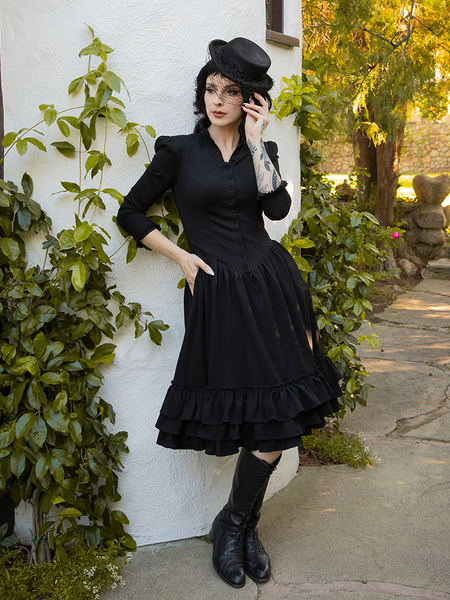 Model adjusts her hair while her other hand rests in the side pocket of the Victorian Dress in Black from gothic glam clothing company La Femme en Noir.