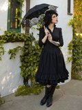 Model looks off in the distance while holding a parasol with ornate flower stitching to keep her Victorian Dress in Black out of the sun.