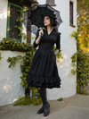 Shot looking upwards, model holds a black parasol while tucking her other hand into the side pocket on her Victorian Dress in Black.