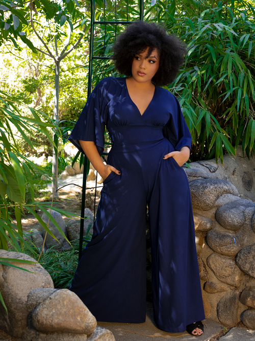 Ashleeta posing in an outdoor garden while modeling the Black Widow Palazzo Pants in Navy along with a matching flowy long sleeve top.