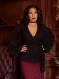 A model, with her hands on her hips, wears the Georgette Wrap Top in Black.