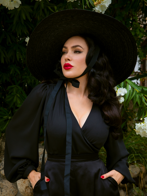 A close-up shot of Micheline Pitt in the Georgette Wrap Top in Black with her hands tucked into her pockets.