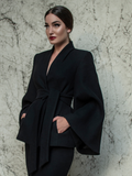 Aliza wearing the Metropolis Suit Jacket in Black in front of a stone wall. 