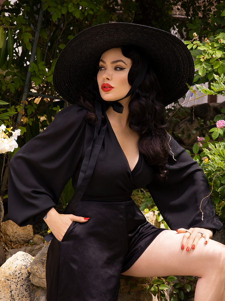 Micheline Pitt standing in the Georgette Wrap Top in Black with a matching black sunhat.
