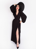 Micheline Pitt photographed while wearing the Black Widow Wrap Gown in Solid Black paired with a oversized black sunhat.