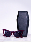 A product photo of the Vamp sunglasses in oxblood with the coffin case by La Femme En Noir.